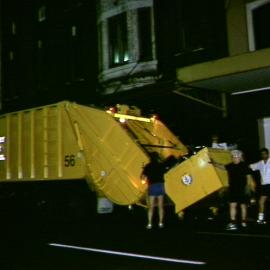 Garbage bin being unloaded into garbage compactor, unknown address, 1989